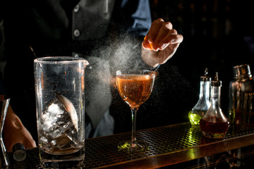close-up of cocktail glass which bartender sprinkling by juice of citrus.