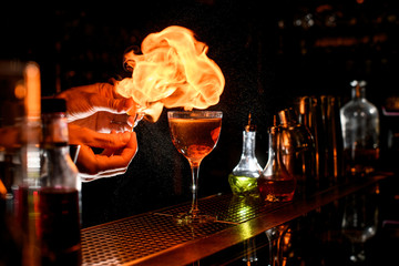 close-up of bartender's hands lighting a flame near glass with cocktail.