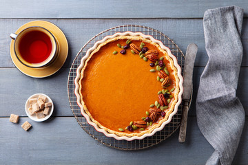Pumpkin pie, tart in a baking dish with cup of tea. Grey wooden background. Top view.