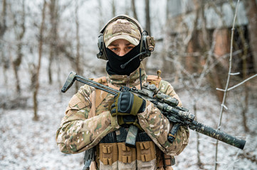 Man in camouflage uniform hold machinegun. Soldier in the winter forest. Horizontal photo side view.