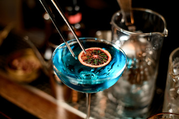 close-up of blue cocktail in wineglass decorated with slice of citrus