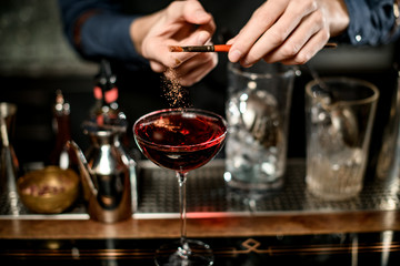 Barman add seasoning to red cocktail in wineglass