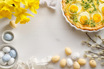 Easter background with quiche with eggs and peas, spring flowers and chocolate eggs on a white background, copy space.