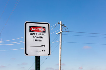 Road sign warning of overhead power lines danger. Electrical transmission wires and pole in...