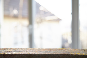 An empty wooden tabletop on a window pane and abstract green blur from the garden with a view of the yard, can be used to display or assemble your products (or products).