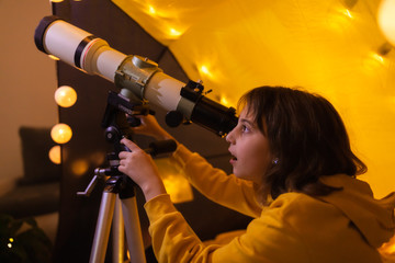 Small girl using telescope at home living room in a tent. © astrosystem