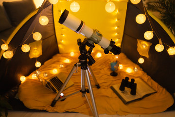 Telescope and child tent in a living room illuminated with lanterns.