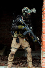 Military man in black uniform with machinegun. Soldier watching someone and stand in the broken...