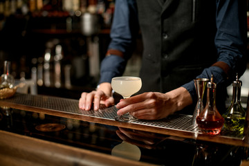 Fototapeta na wymiar bartender in blue shirt holding white cocktail in glass on the bar