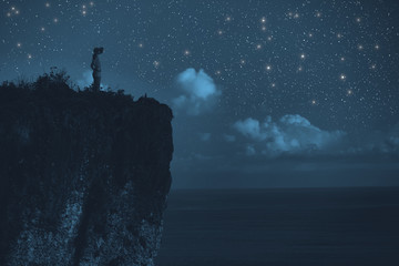 Silhouette of a woman with milky way stars above the ocean horizon.