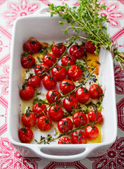 Roasted cherry tomatoes with herbs in baking dish. Close up.