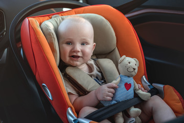 Smilimg baby boy with a bear toy sitting in the car seat. - 328730627