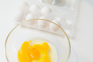 Yellow yolk with broken egg protein in a deep plate next to a pack of a dozen eggs and flour before cooking on a white isolated background.