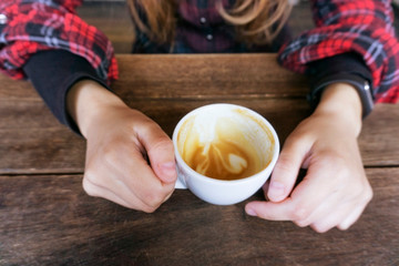 Female in red shirt holding espresso cup with some coffee and foam it in on wooden table, top view