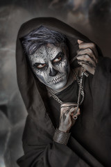 Fototapeta na wymiar Close up portrait of terrible guy with Halloween skull face painting. Professional makeup. Chain in hands