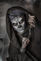 Close up portrait of terrible guy with Halloween skull face painting. Professional makeup. Chain in hands