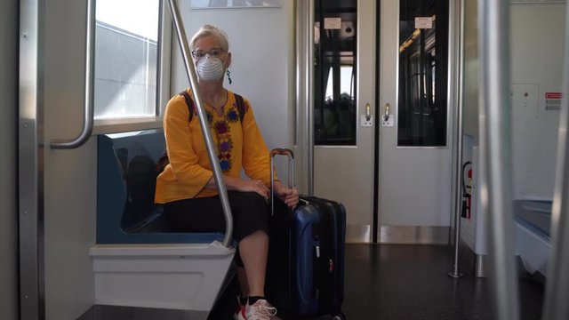 Closeup of woman wearing protective breathing mask adjusting luggage on a moving train at an airport.