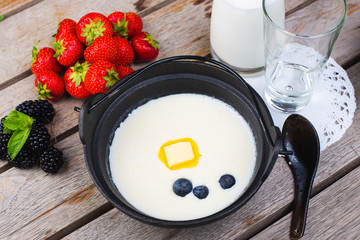 Traditional breakfast milk porridge with butter and berries on a wooden table.