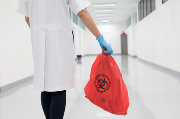 Scientist wearing blue gloves and red bag with bioharzard sign.A woman worker hand holding red garbage bag.Maid and infection waste bin at the indoor public building.Infectious control.