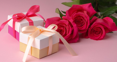 gift boxes multicolored with satin ribbons and three pink floyd roses on a pink background