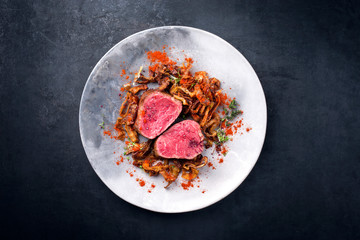 Gegrilltes dry aged Filet Medaillon Steak natur vom Rind mit gerösteten Zwiebelringen und Karotten als Draufsicht auf einem Modern Design Teller mit Textfreiraum