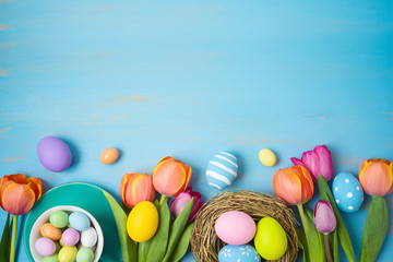 Easter holiday background with easter eggs and tulip flowers on wooden table.