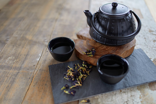Herbal asian tea on vintage wooden table. Top side view of teapot and cups on black rock with copy space