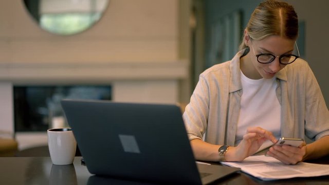 Millennial Generation Y in spectacles searching medial files for download from blog websites connected to 4g wireless on cellphone,female student sitting at table with netbook and doing mobile texting