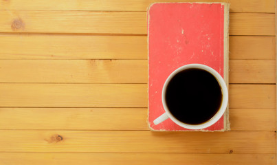 Top view, A cup of coffee and closed red book on wooden background.