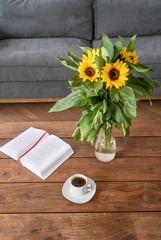 Sunflower bouquet in vase, book and cup of coffee. Still nature in luxury living room
