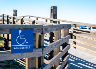 Sign on a wooden handicapped accessible ramp for use by the disabled next to a car parking lot.