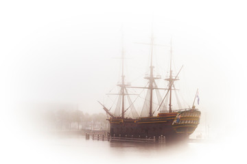 Old wooden dutch galeon in harbour. High key image of vintage battleship in a fog.