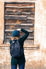 Girl photographer with a backpack, on the street in a green hat and jacket photographs a clogged (boarded up) board with an old window. Back view, vintage photo