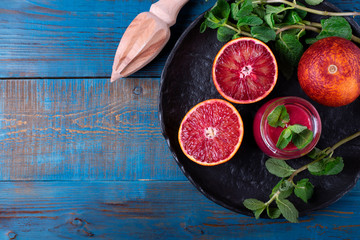 Blood oranges and wooden squeezer against the blue background. Top view. Copy space