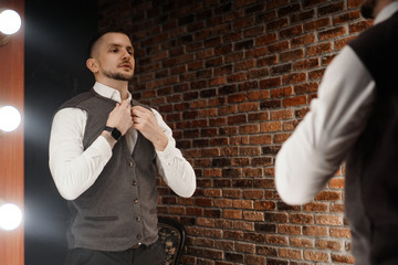 Stylish confident young man looking at himself in mirror. Fitting a suit in a store or sewing studio - loft interior