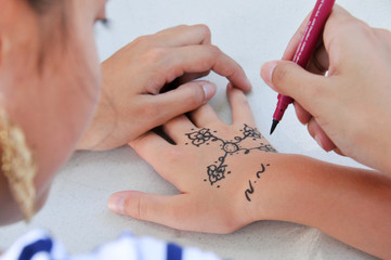 Détail d'une jeune femme dessinant au henné un tatouage sur le dos de la main d'une petite fille