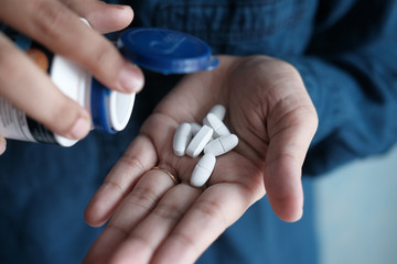 Pouring the pills from the white bottle into the hand .