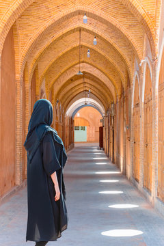 Beautiful Iranian girl standing wearing abaya in the narrow street of old adobe Yazd city - IRAN