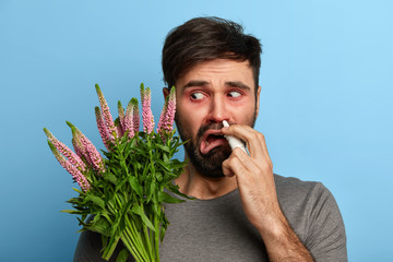 Unhappy man feels unwell, being allergic to pollen, suffers from allergy to plants, uses nasal...