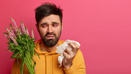 Allergy, sickness, bad feelings concept. Upset ill guy suffers from allergy on flower pollen, holds...