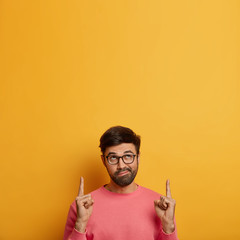 Vertical image of intrigued bearded man points fore fingers above, purses lips and shows something...