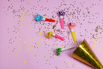 Birthday or party colorful happiness background with party noise whistles, birthday hat and confetti on pink background. Carnival air blowers flat lay, top view image.