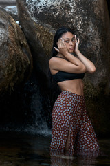 Joven morena de pelo de pie posando junto a las rocas en las montañas mojada dentro del agua...