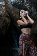 Joven morena de pelo de pie posando junto a las rocas en las montañas mojada dentro del agua...
