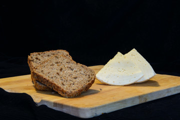 Bread with sunflower seeds and a piece of cheese lie on a cutting board. Black background. Concept - healthy food, diet.