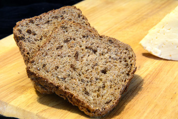Bread with sunflower seeds and a piece of cheese lie on a cutting board. Black background. Concept - healthy food, diet.