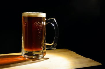 Beer mug with dark beer on a black background, illuminated by a lamp. Bubbles in a liquid. Concept - natural product, pub, splash