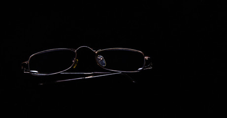 Glasses in a gold frame lie on a black background. Concept - minimalist black, business