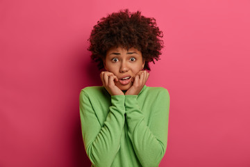 Fototapeta na wymiar Photo of worried nervous woman looks puzzled, afraids of saying something, dressed in casual wear, isolated over pink background, has concerned expression, feels frightened. Face expressions