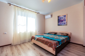 A room in the guest house with a large wooden bed with a beige and blue bedspread. The room has a window, wardrobe and split
